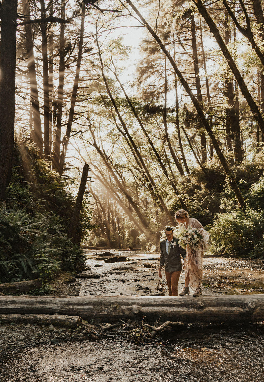 bride and groom hiking through redwoods at their adventure elopement with the sun shining through the trees