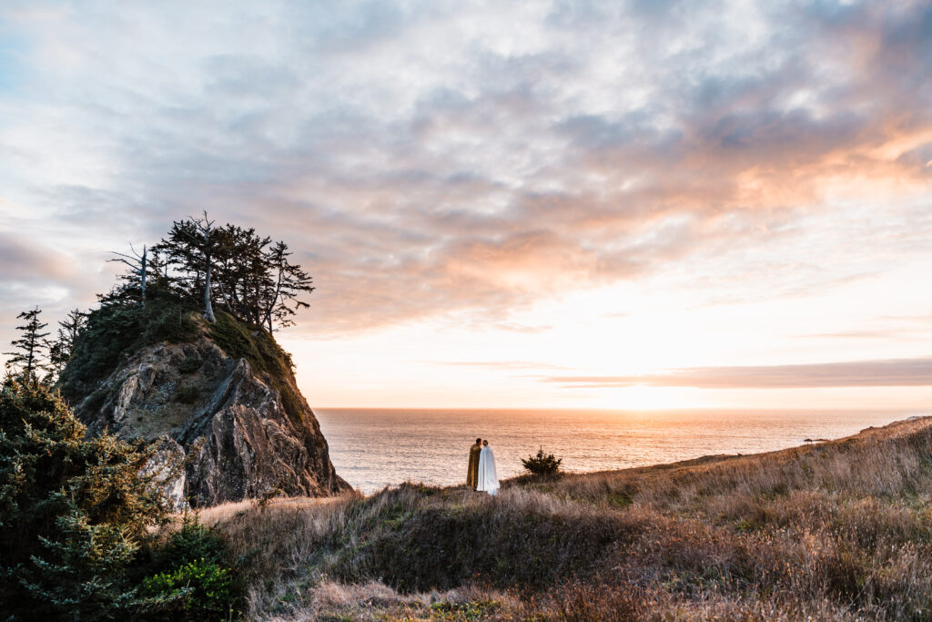 couple dressed in capes and fantasy attire looking at a beautiful sunset over the ocean